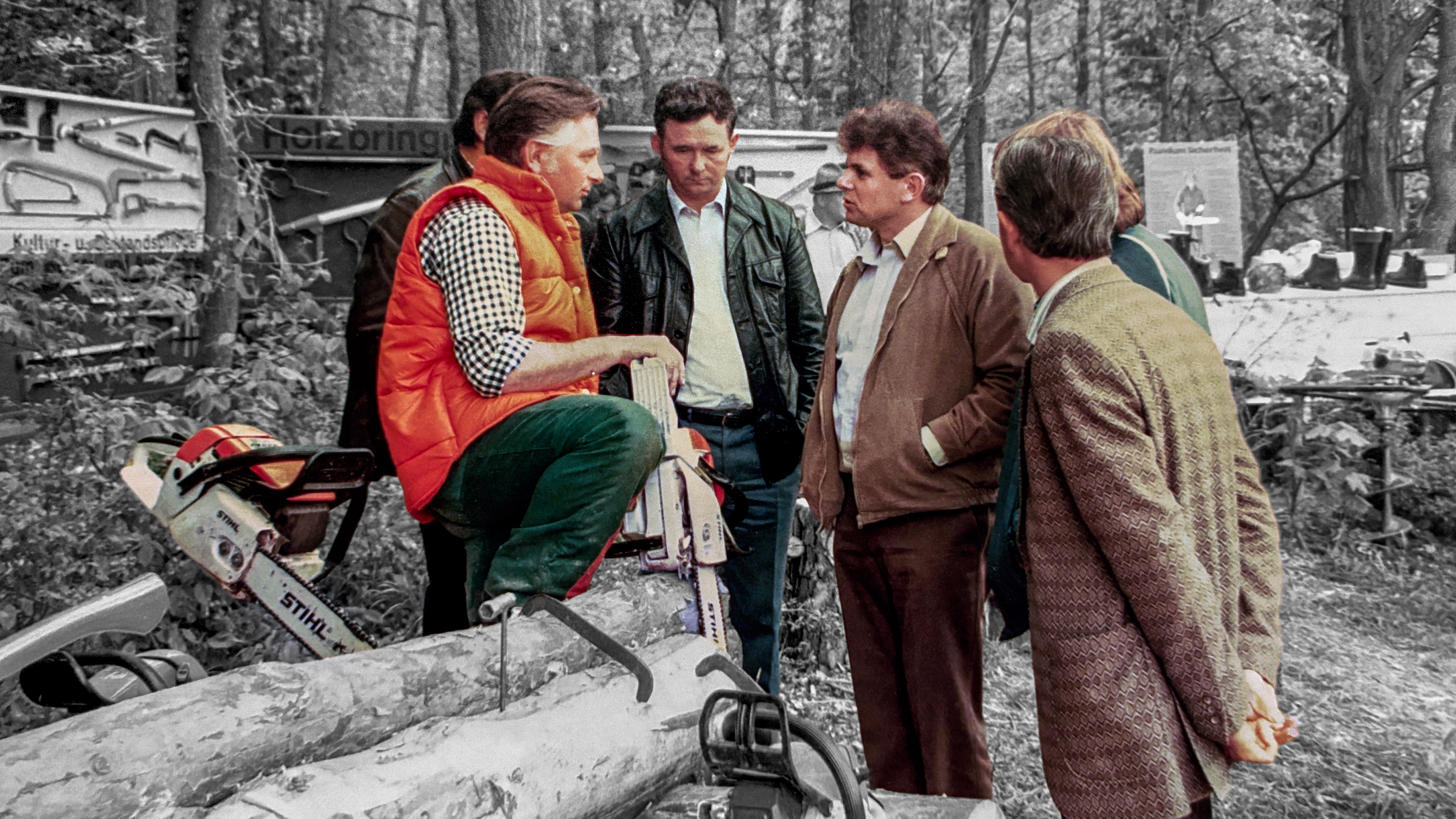 A group of men in the forest; one is wearing an orange vest.