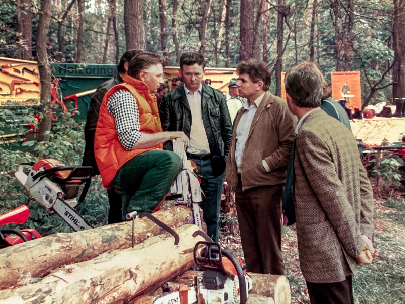 A group of men in the forest, one is wearing an orange vest.