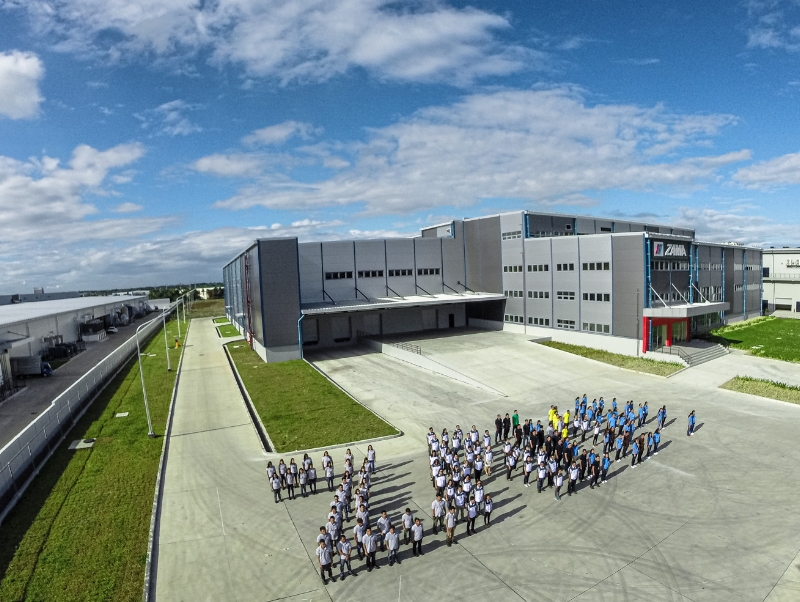 People in the shape of the word ZAMA, a factory in the background.
