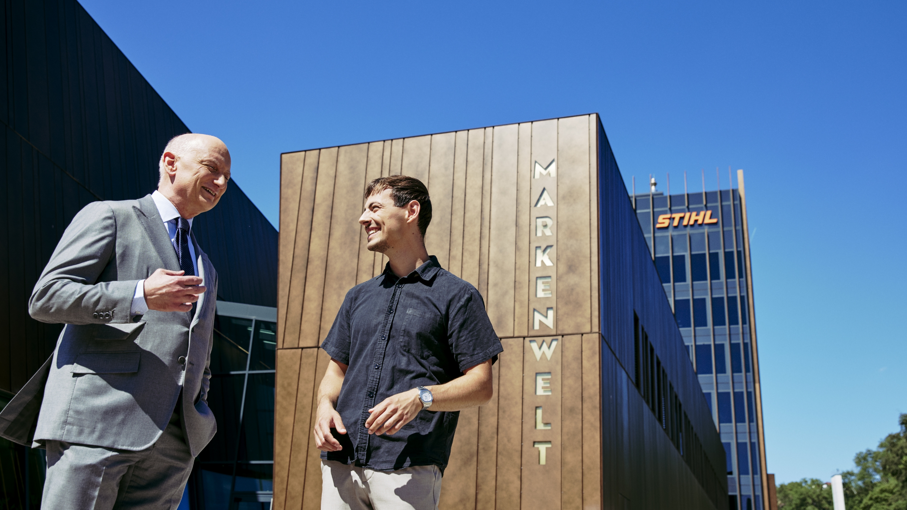 Dr. Nikolas Stihl and Tamino Soubawi talk in front of a modern building with the signs &ldquo;Brand World&rdquo; and &ldquo;STIHL&rdquo;.