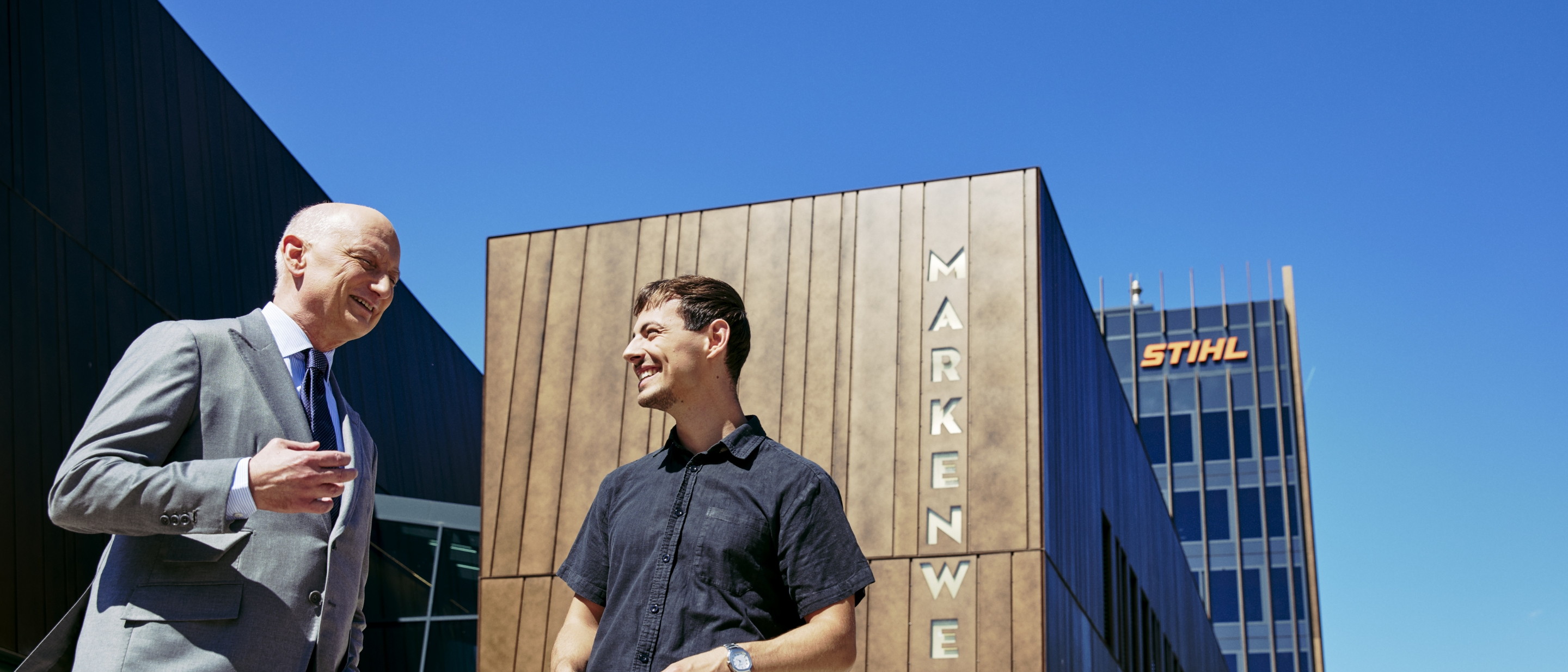 Dr. Nikolas Stihl and Tamino Soubawi talk in front of a modern building with the signs &ldquo;Brand World&rdquo; and &ldquo;STIHL&rdquo;.