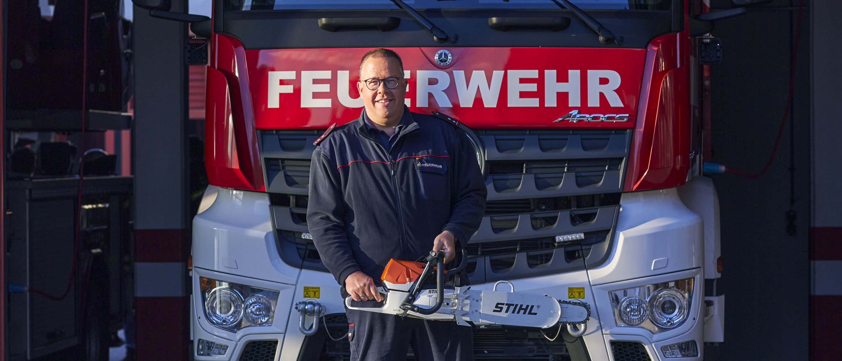 A man showcasing a STIHL chainsaw, with a fire truck behind him.