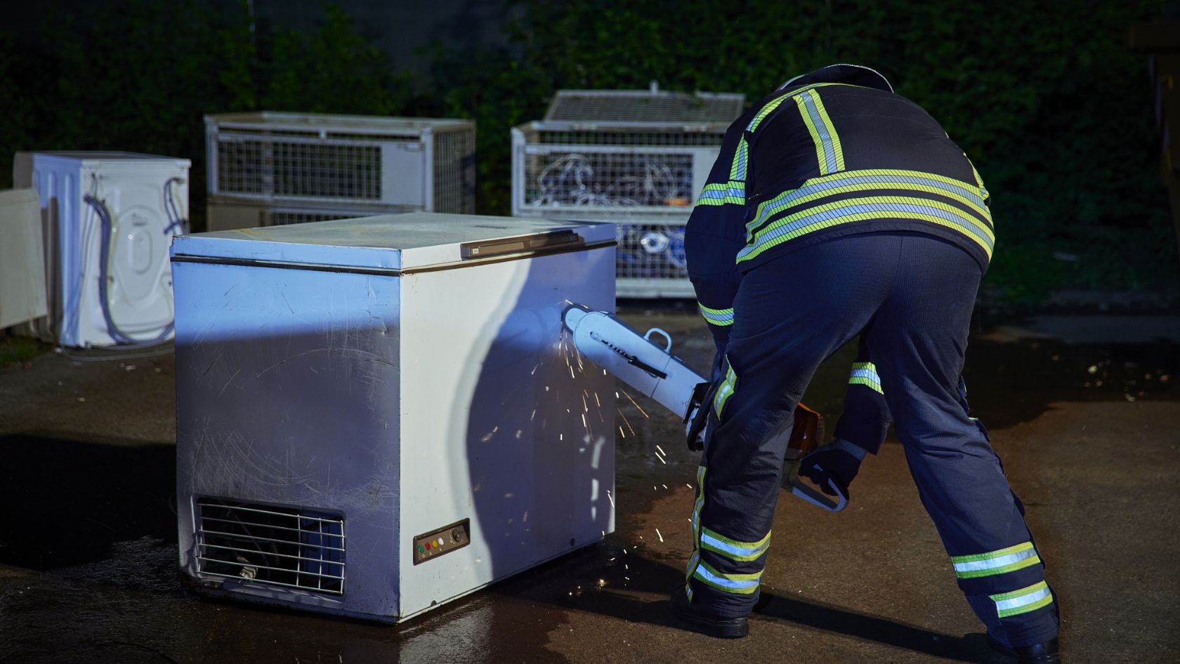 A firefighter gets to work on a freezer box with a chainsaw.