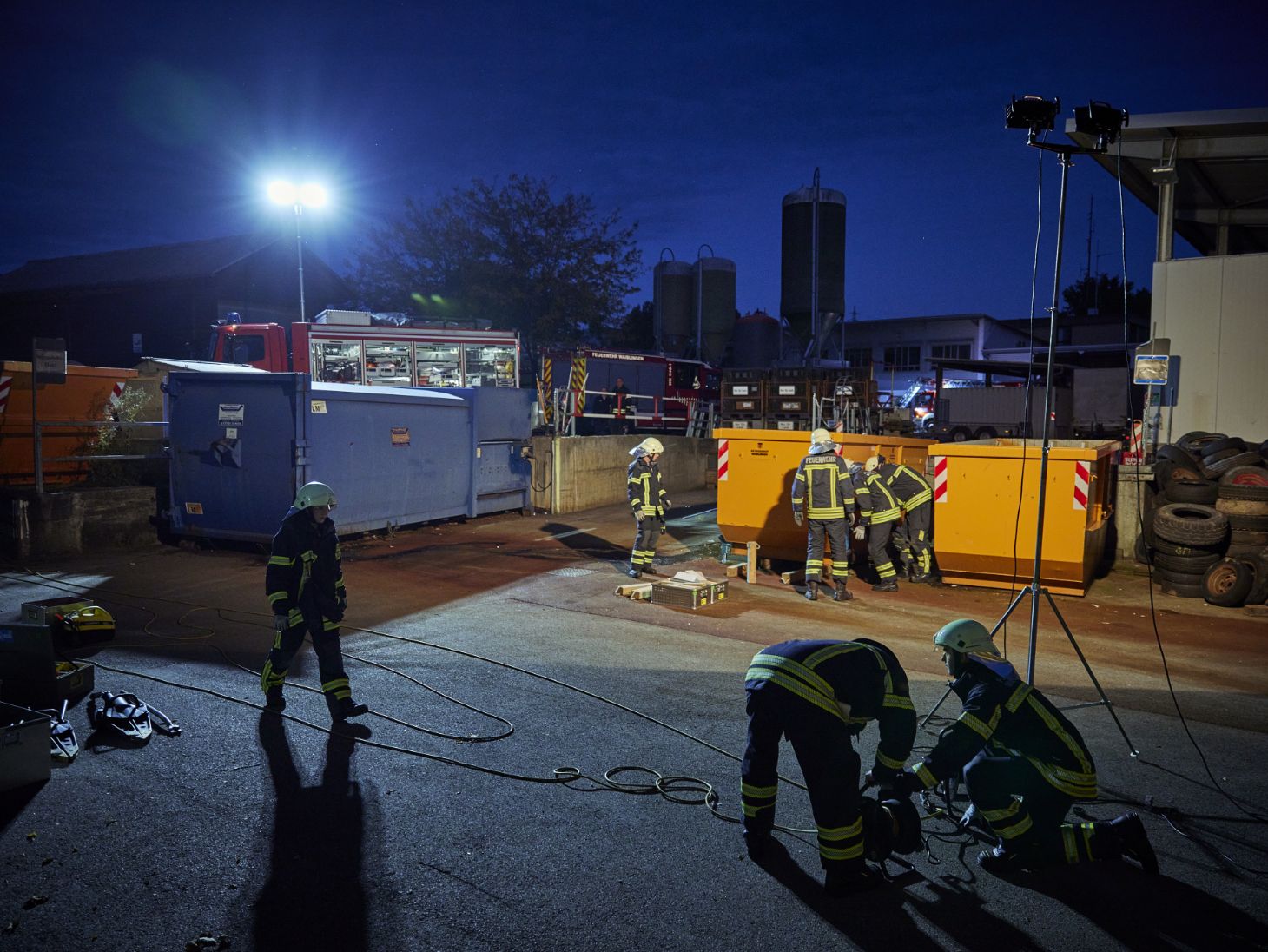 Firefighters standing in front of two containers illuminated by a spotlight.