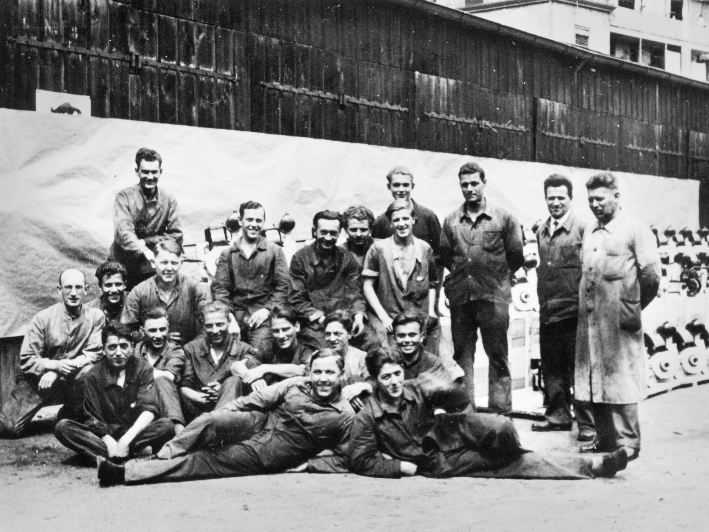 A group of men in front of a large number of gasoline chainsaws; black and white photo.