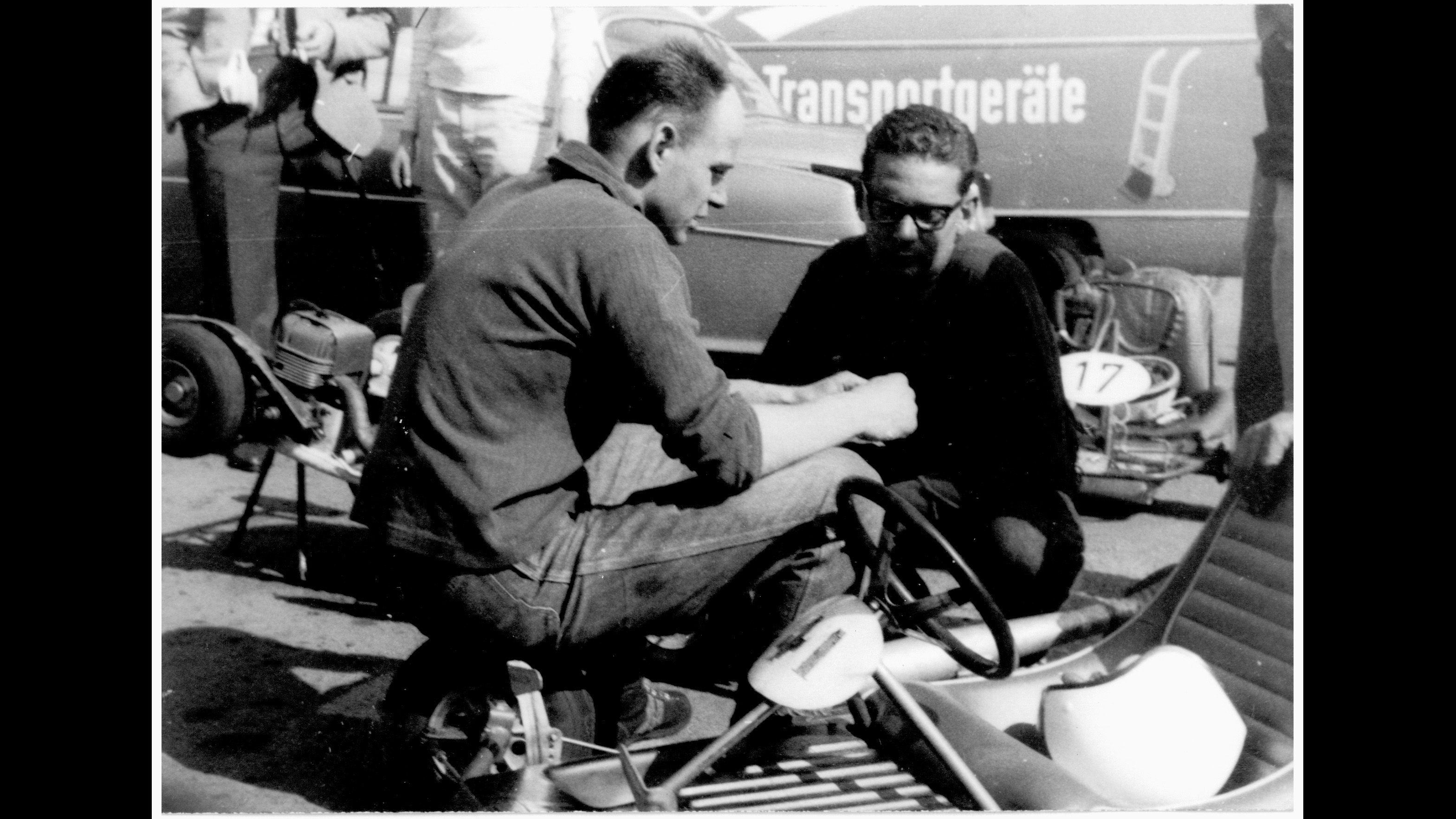 Two men confer at a go-kart race; black-and-white photo.