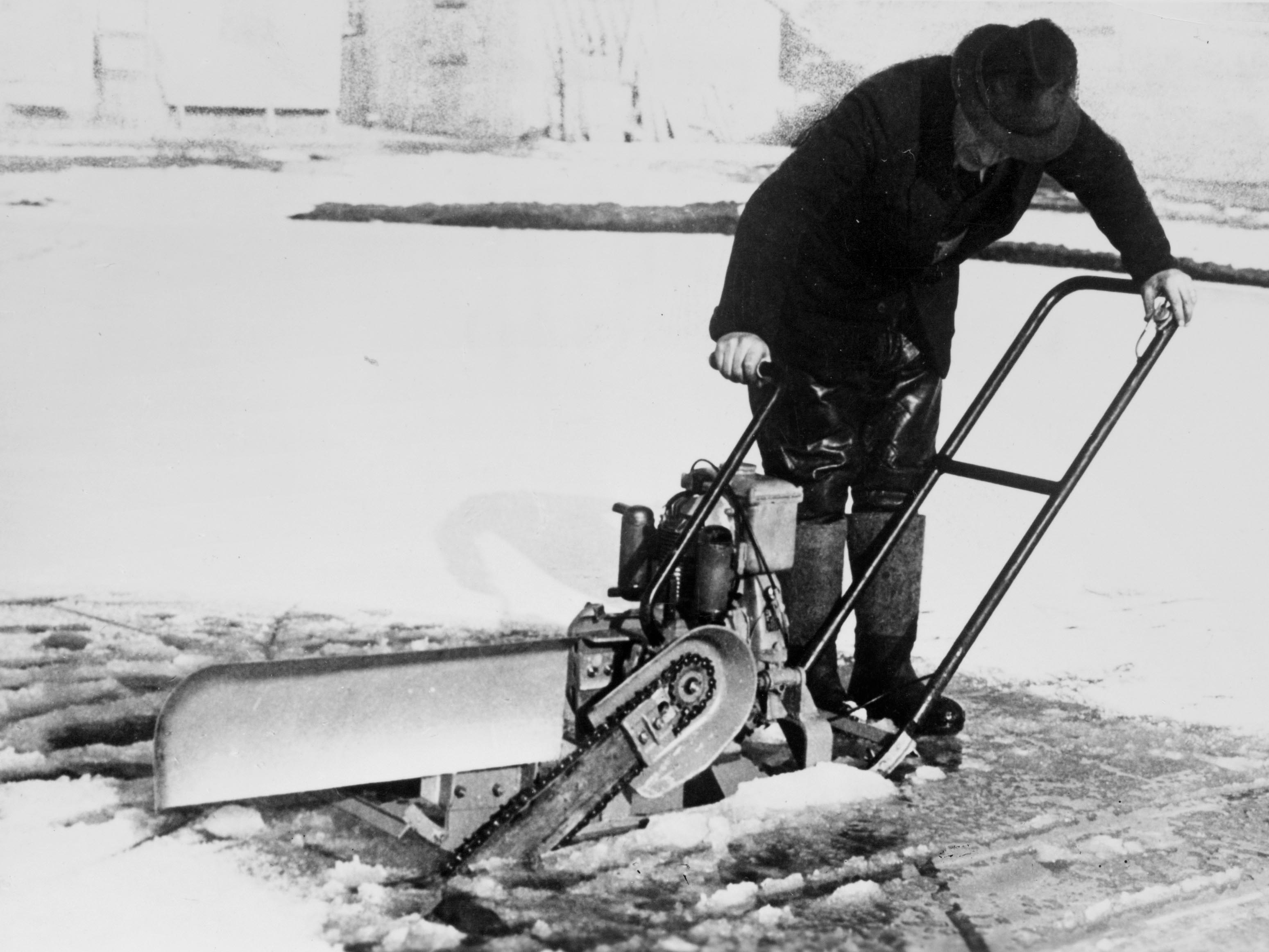 Cut-out ice saw pierces ice cover; black-and-white photo.