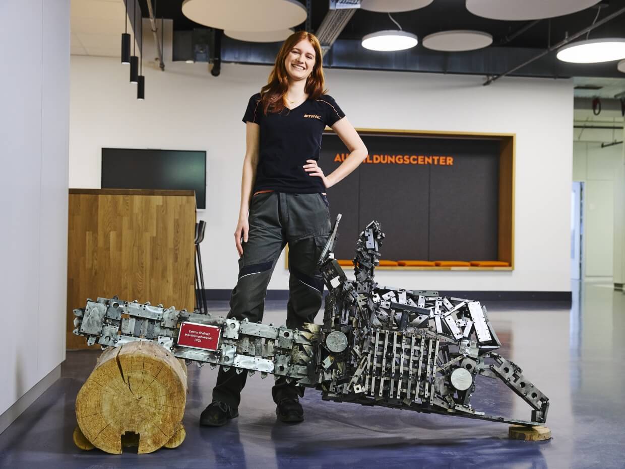 A young woman standing behind a larger-than-life model of a chainsaw.
