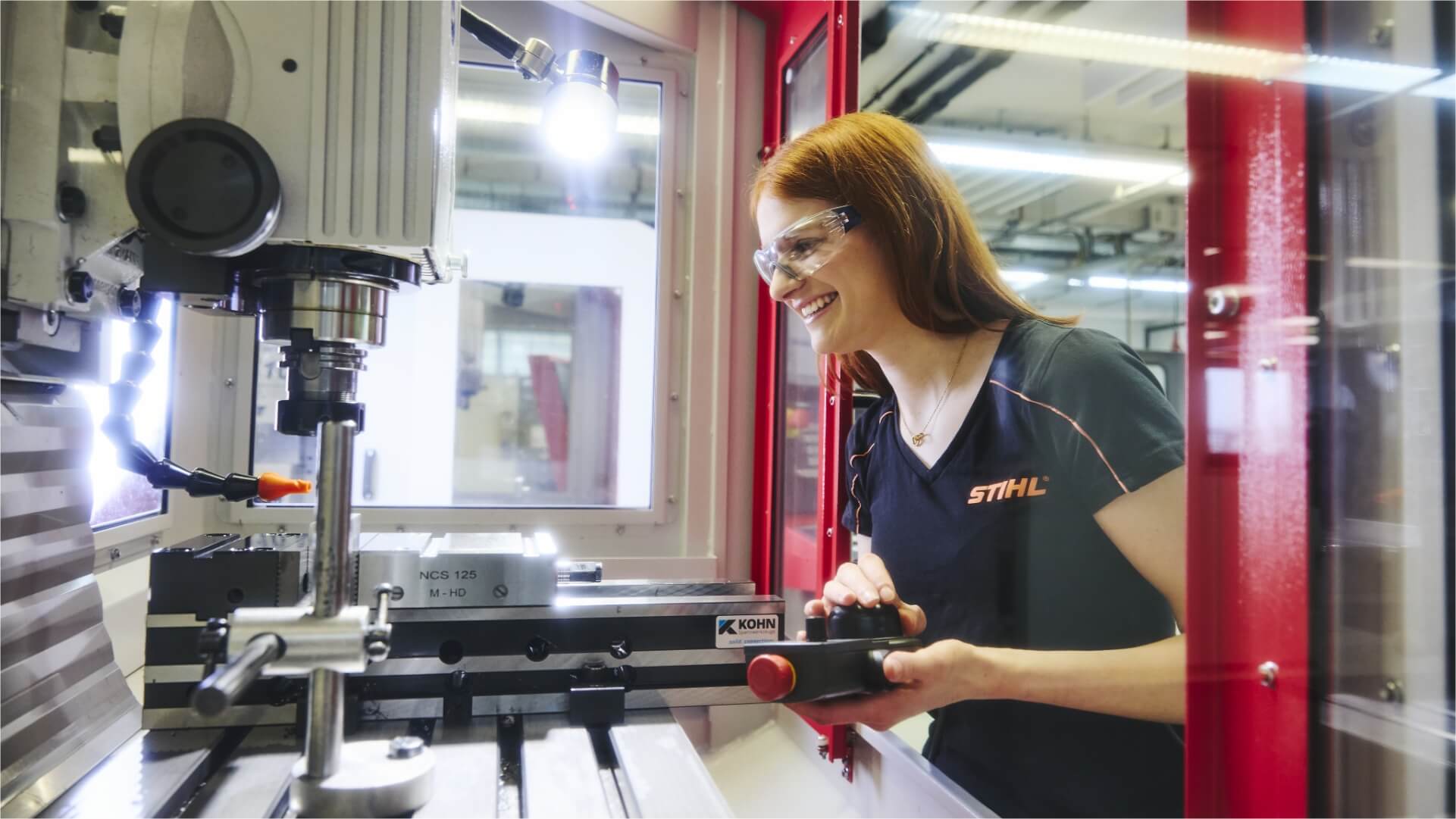 A young woman wearing safety glasses operating a milling machine with a remote control.