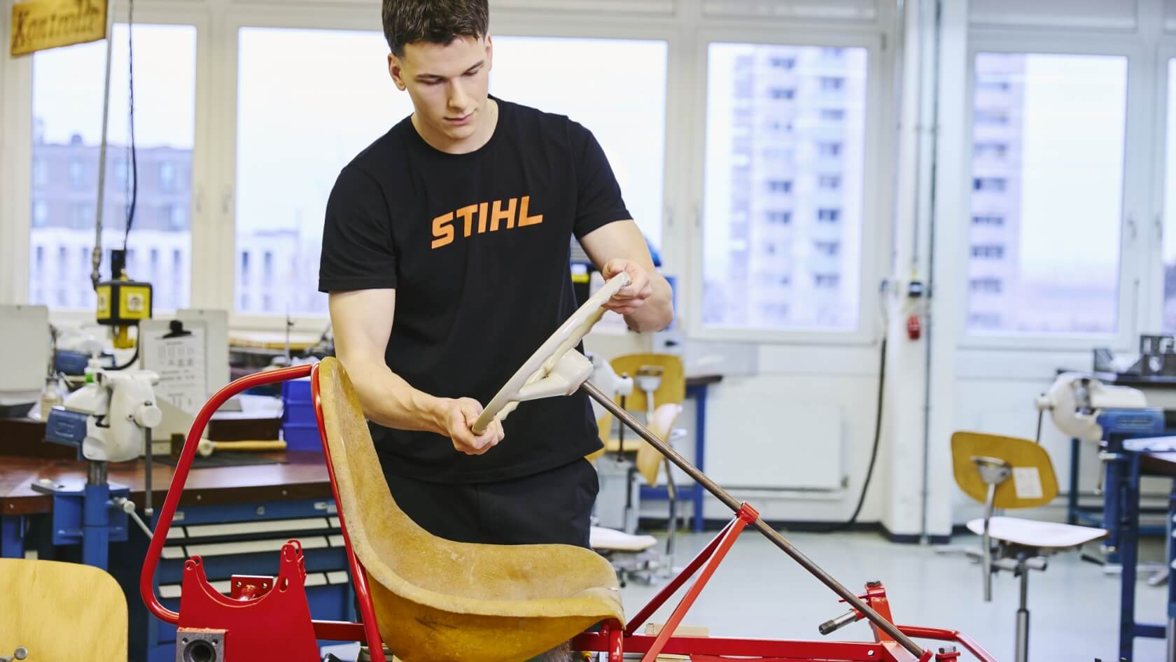 A young man fits the steering wheel onto a red-painted go-kart frame